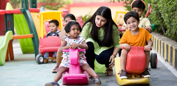 Female teacher with preschool children riding toy rocking horse